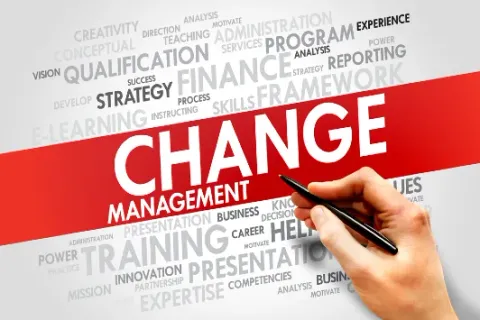The words Change Management on a red band, surrounded by a word cloud of training and business terms, with a hand holding a pen